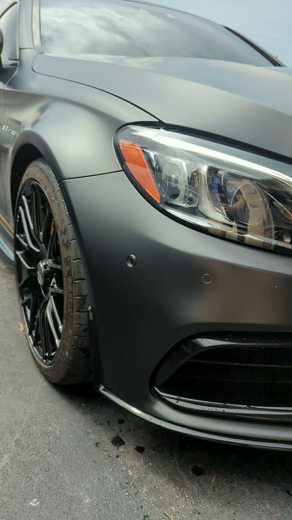 Matte black sports car close-up showcasing sleek design and black alloy wheels.