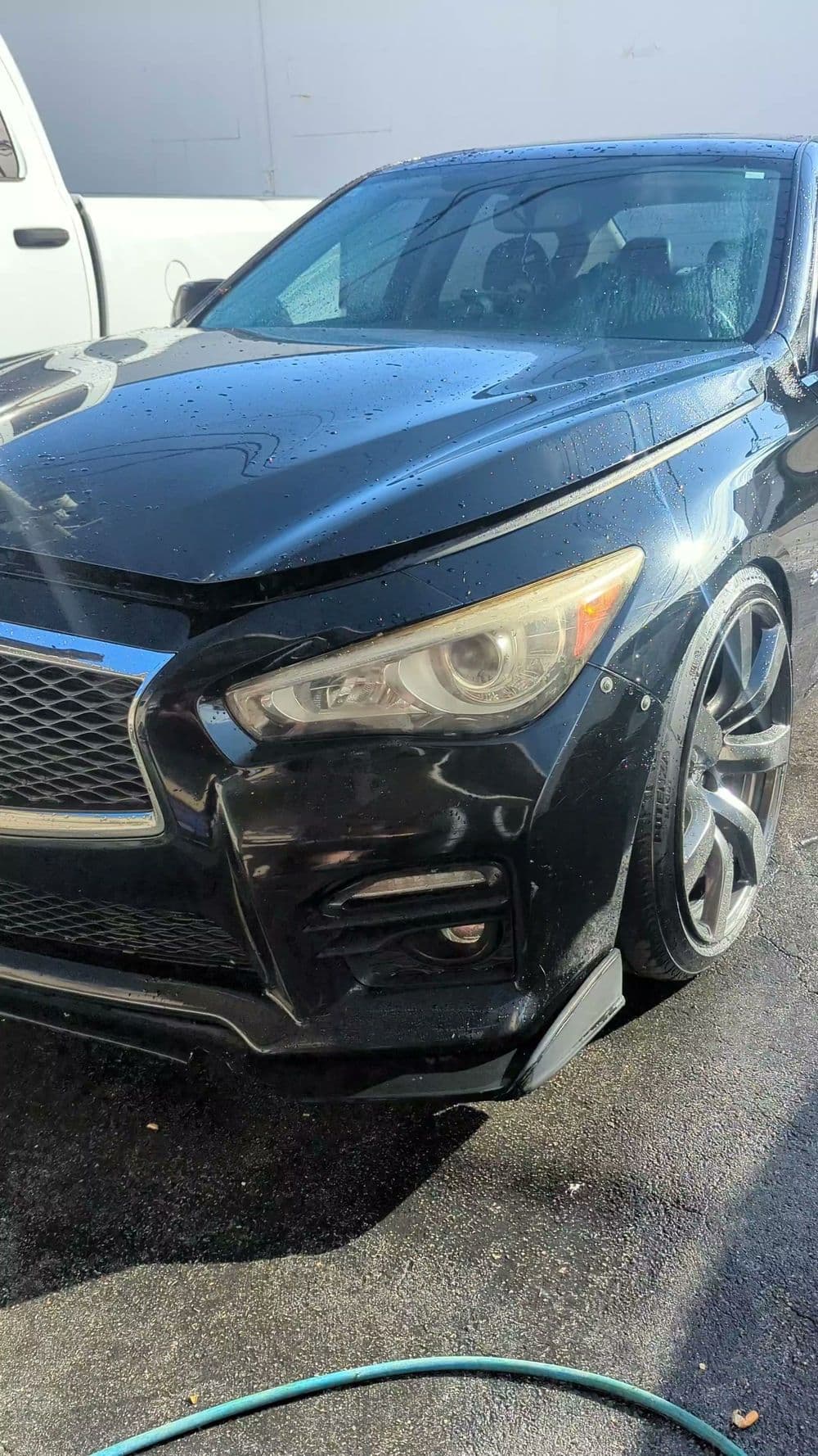 Black luxury sedan with prominent grille, clean surface, and shiny alloy wheels in bright sunlight.