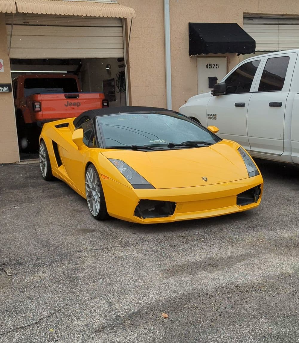 Yellow Lamborghini Gallardo Spyder parked outside a garage, showcasing its sleek design.