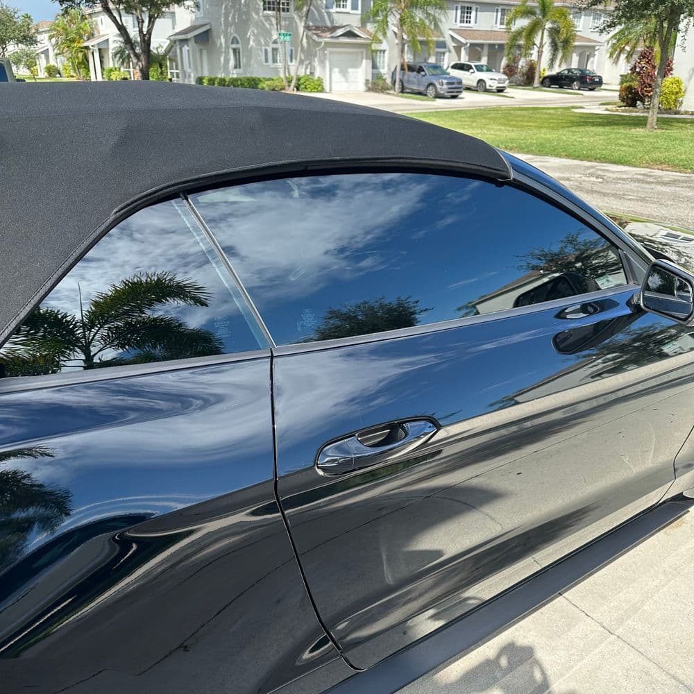 Black convertible car with a soft top parked in a sunny neighborhood with palm trees.