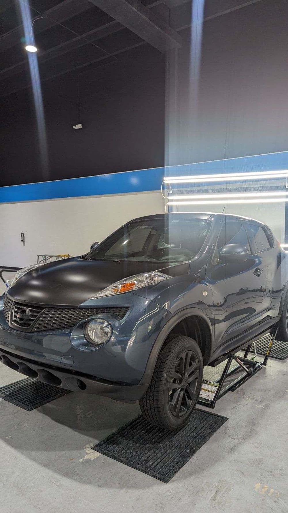 Nissan Juke SUV in a garage on a lift, showcasing its sleek design and matte finish.