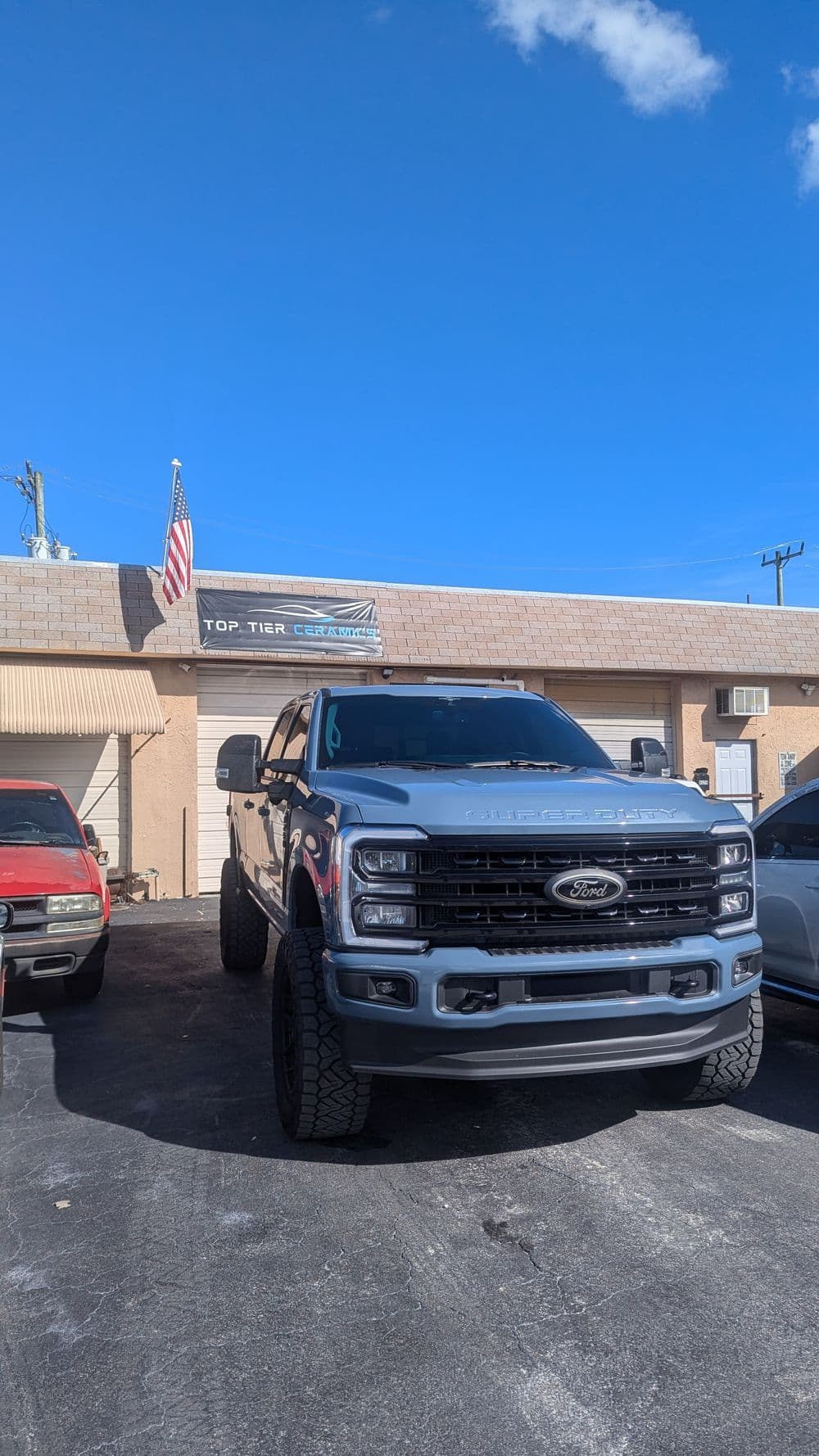Silver Ford truck parked in front of Top Tier Customs shop under a clear blue sky.