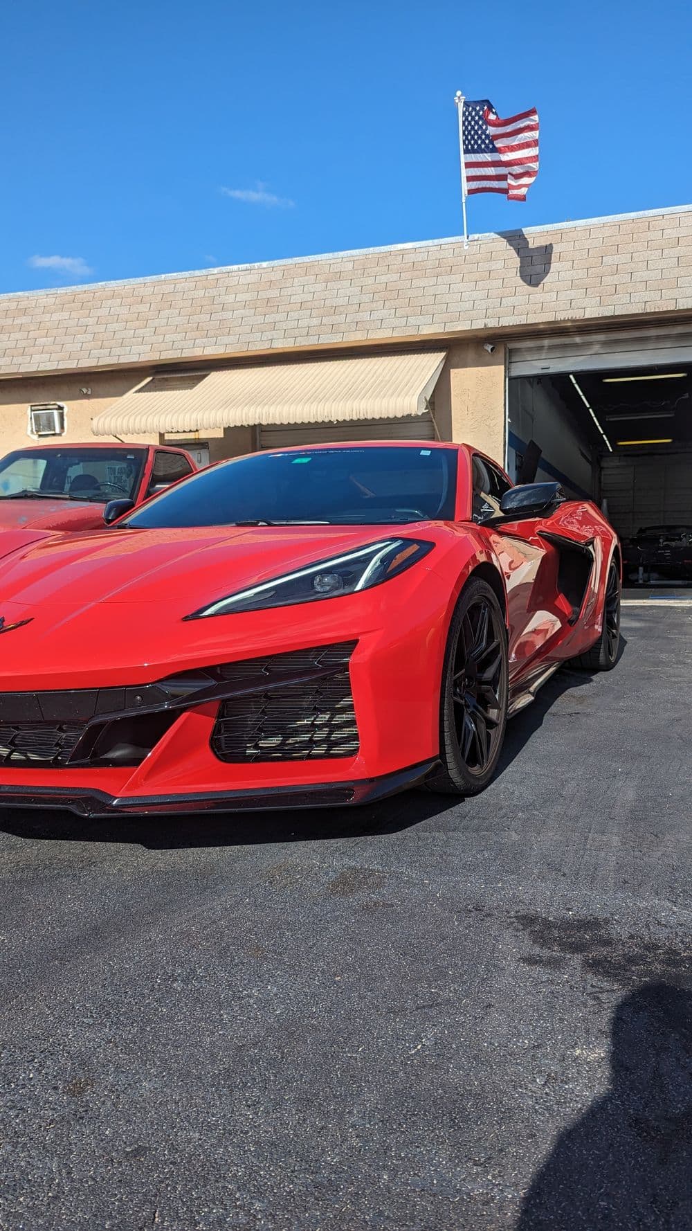 Red Corvette C8 Stingray parked outside a garage with an American flag in the background.