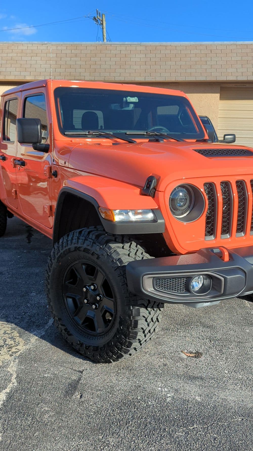 Bright orange Jeep Wrangler with custom black rims parked in a sunny outdoor setting.