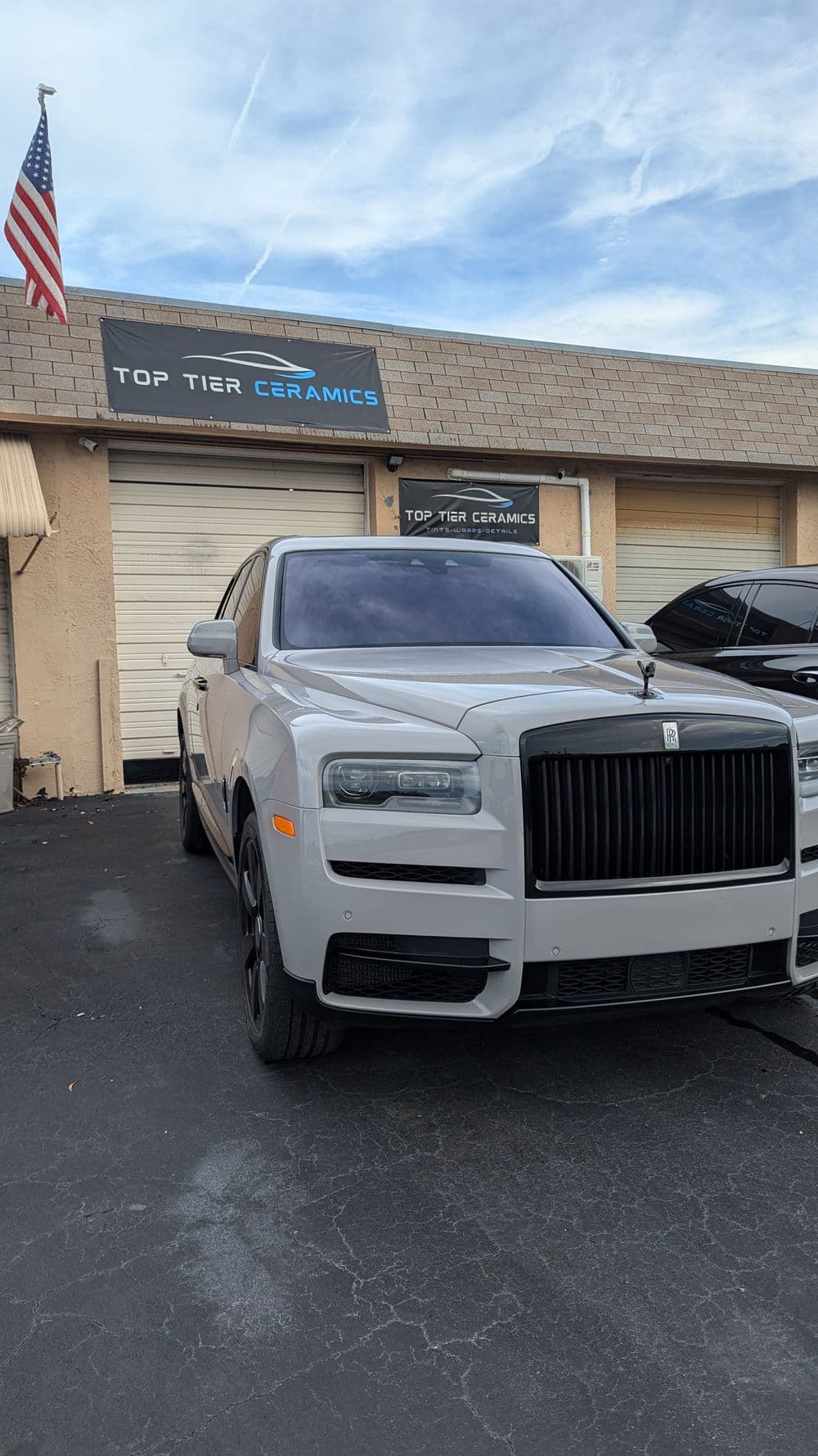 Rolls-Royce SUV parked in front of Top Tier Ceramics with American flag in background.