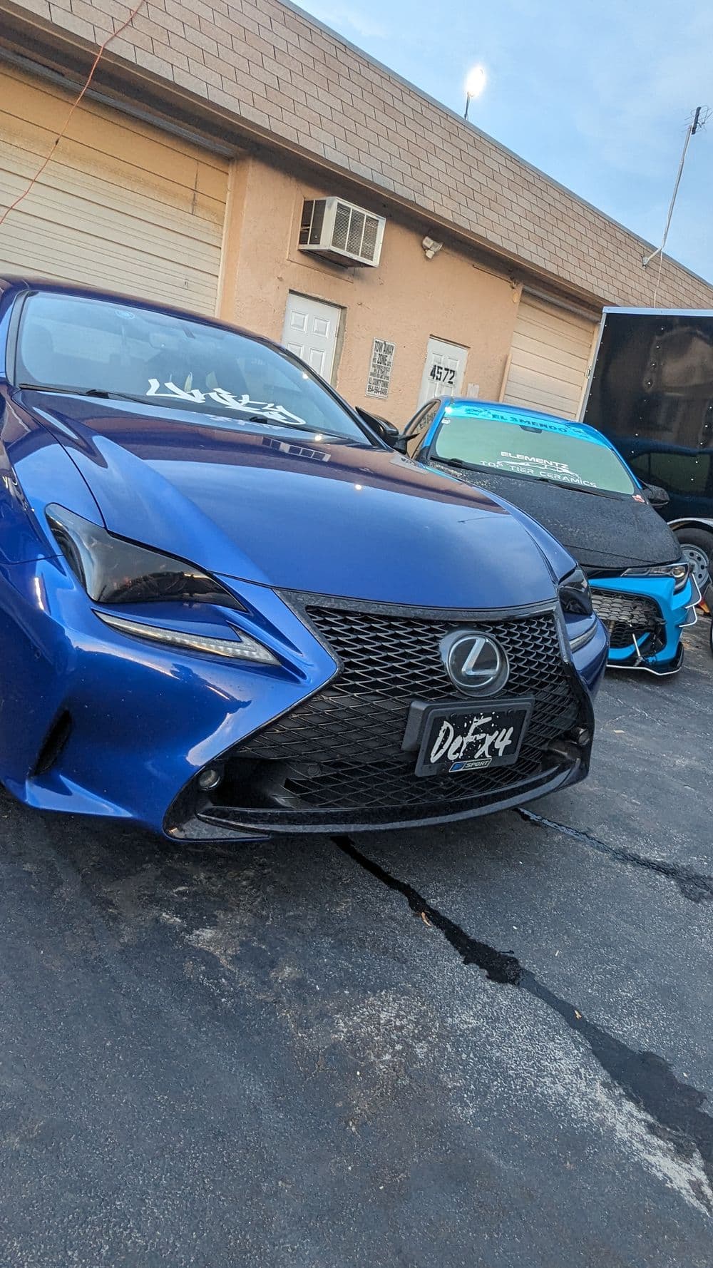 Blue Lexus with custom grill parked near another modified car in a garage setting.