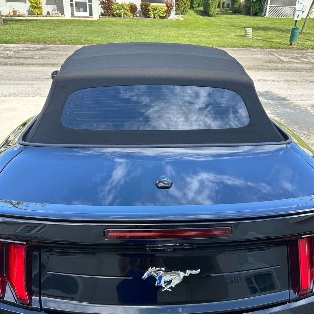 Black convertible Mustang with a soft top parked in a residential area under a blue sky.