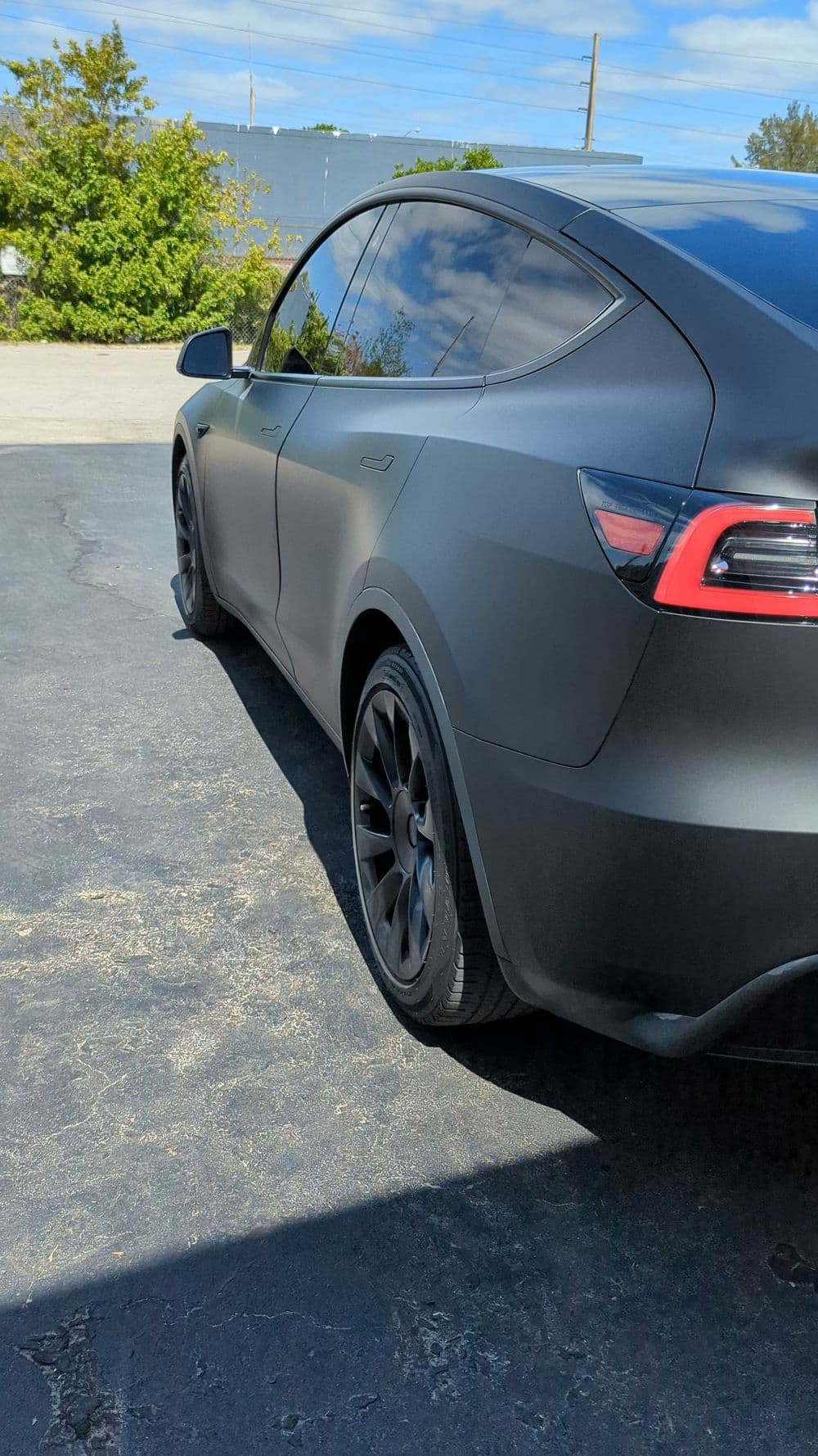 Matte black Tesla Model Y parked with sleek design and modern rims under blue sky.