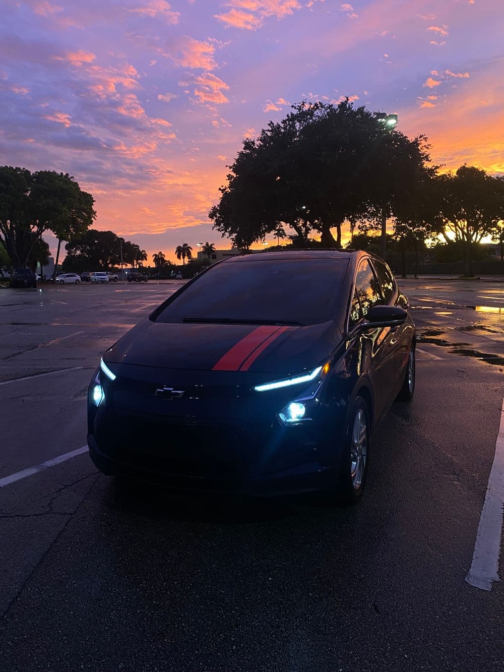 Chevrolet Bolt EV parked under a colorful sunset, showcasing its sleek design and modern headlights.