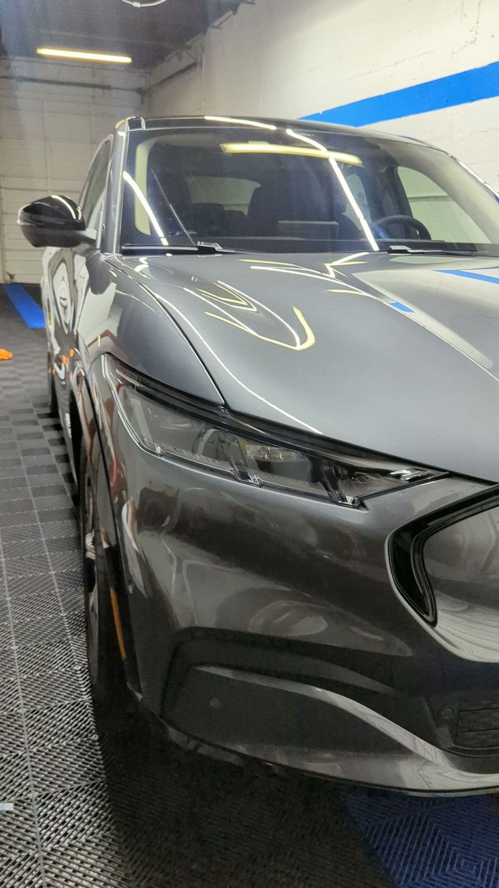 Gray luxury sedan parked in a modern garage with blue accents and clean floor tiles.