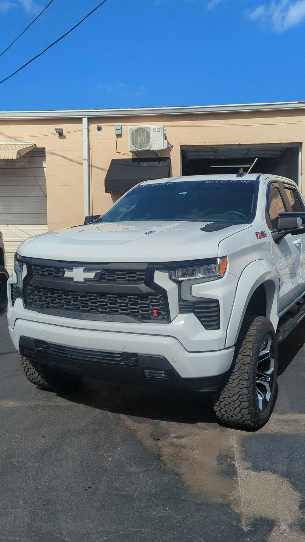 White Chevrolet Silverado truck with aggressive front design and large tires, parked outdoors.