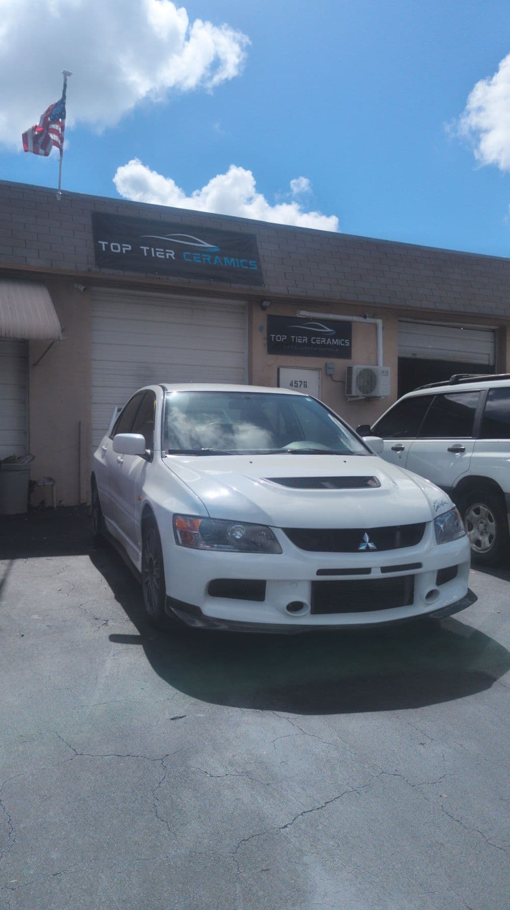 White Mitsubishi car parked outside Top Tier Ceramics shop under a clear blue sky.