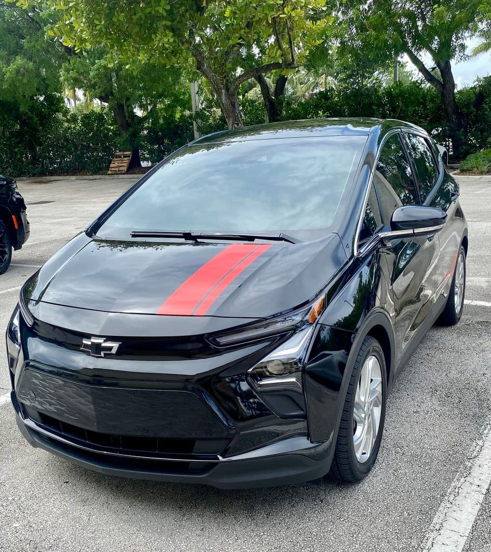 Black Chevrolet Bolt EV with red stripe parked in a lush green area.