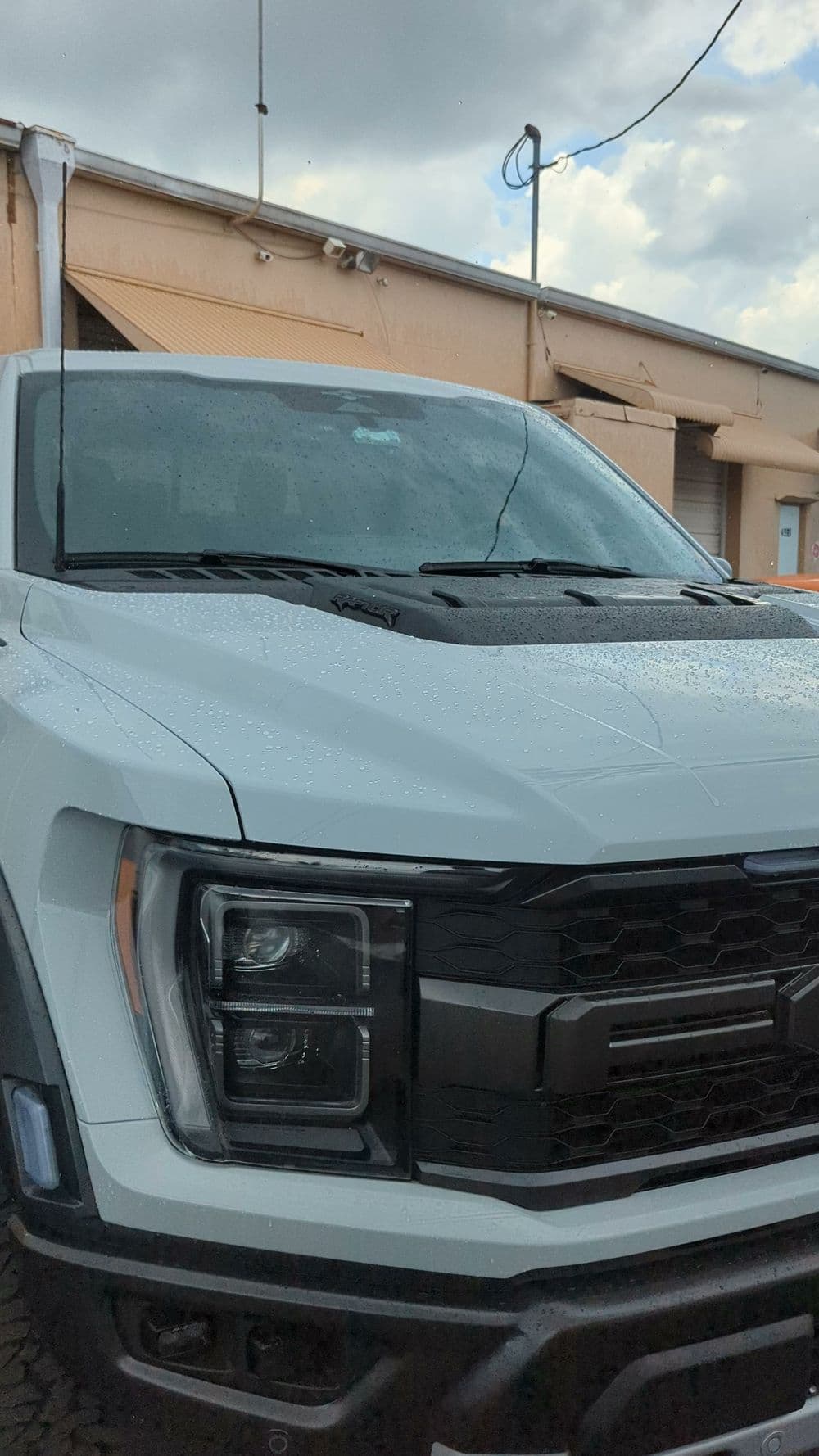 Front view of a sleek white pickup truck with a black grille and raindrops on the hood.