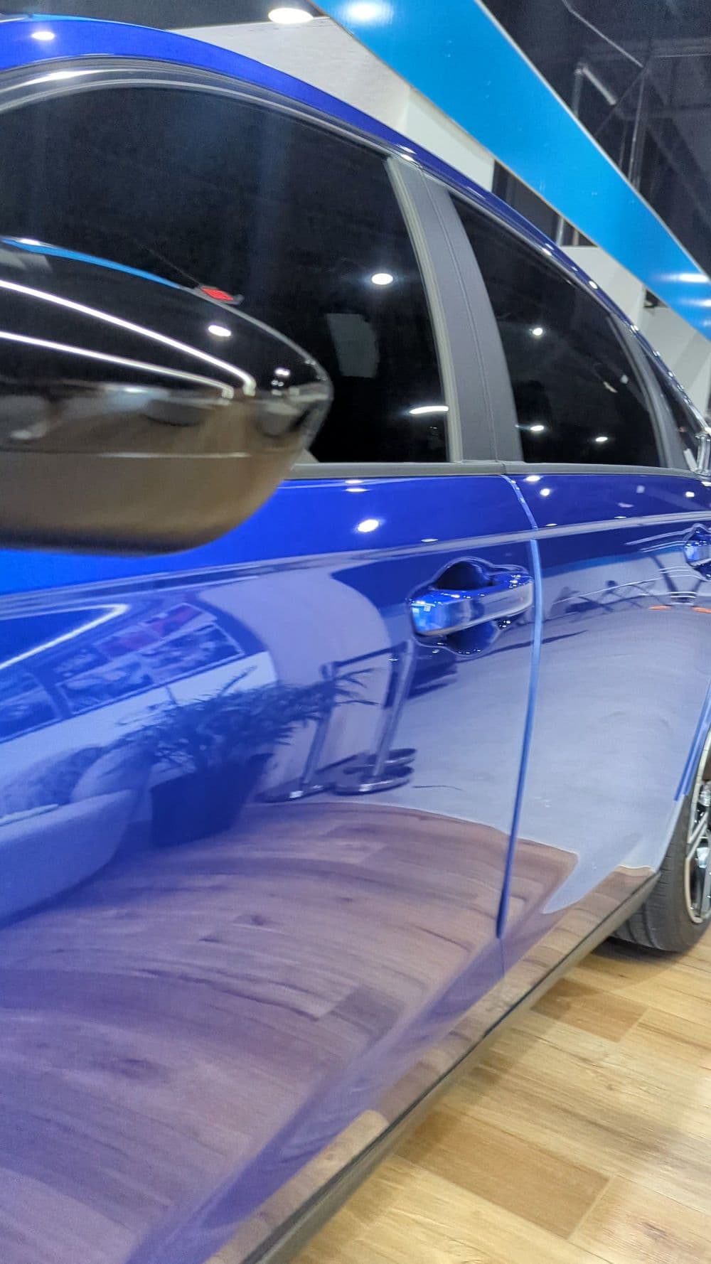 Blue car with tinted windows showcased in a modern indoor setting reflecting details around it.