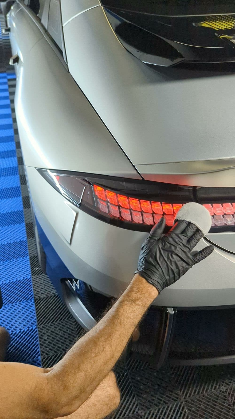 Person detailing a modern car's rear light with a microfiber cloth. High-quality auto detailing.