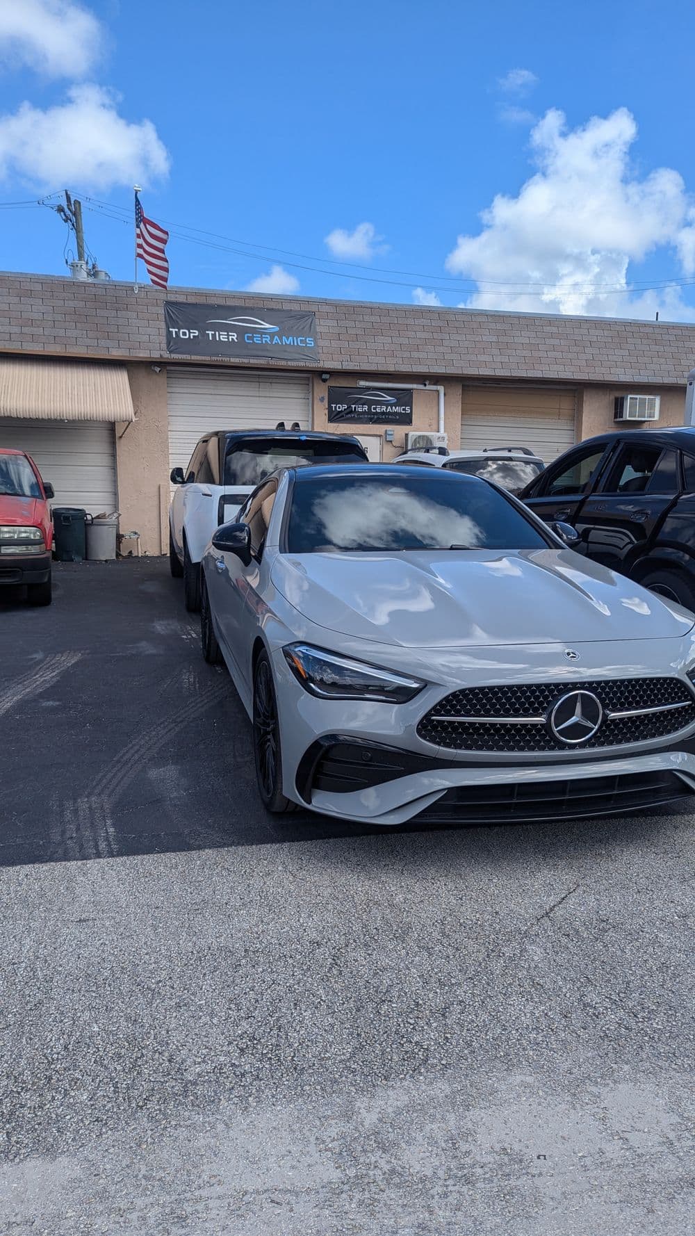 Mercedes-Benz car parked in front of Top Tier Ceramics shop with blue sky and American flag.