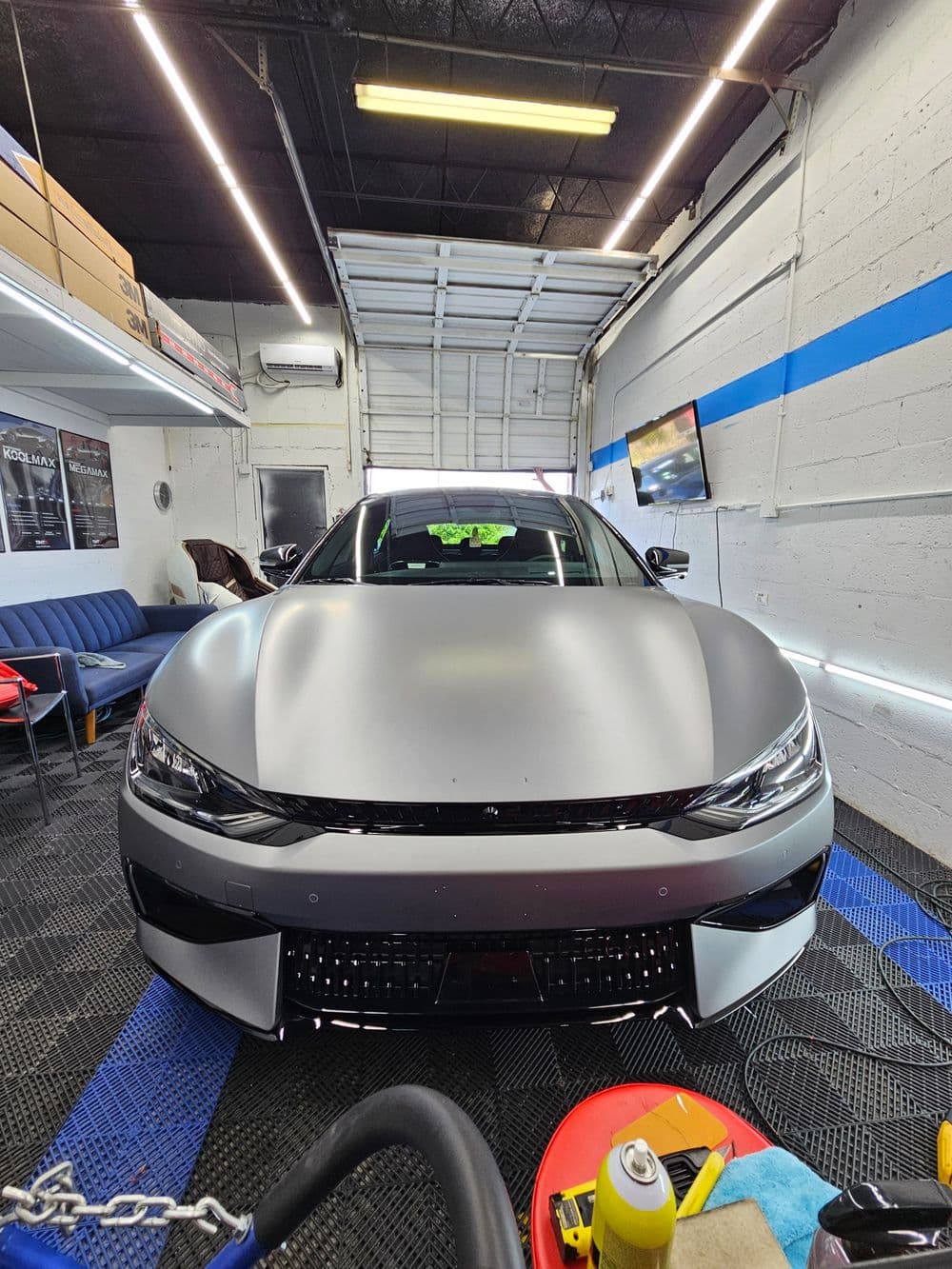Sleek matte gray car in a modern garage with tools and equipment in the foreground.