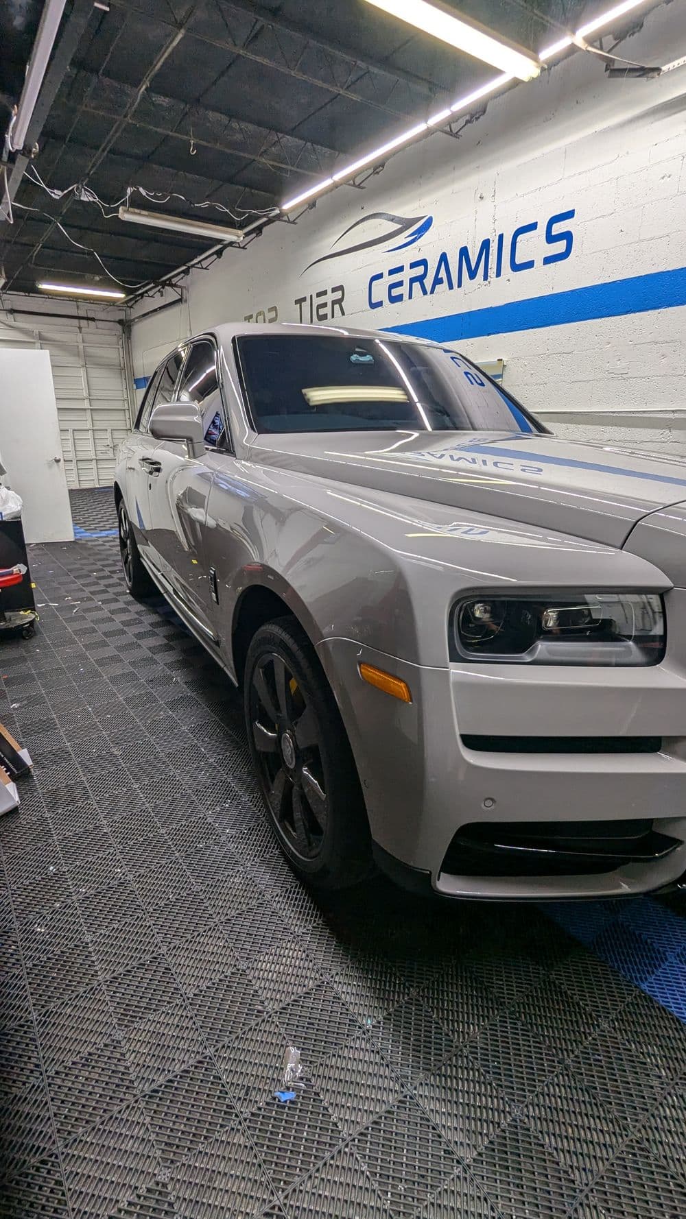 Luxury silver Rolls Royce parked in a detailing shop with blue and white wall branding.