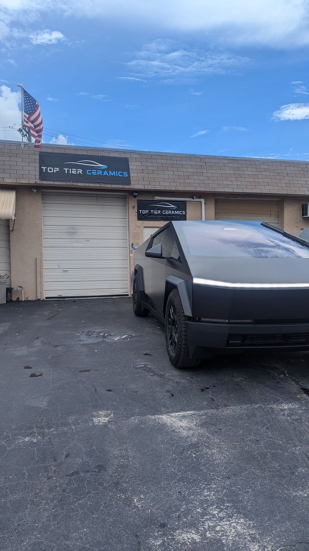 Futuristic electric vehicle parked outside Top Tier Ceramics store with American flag.