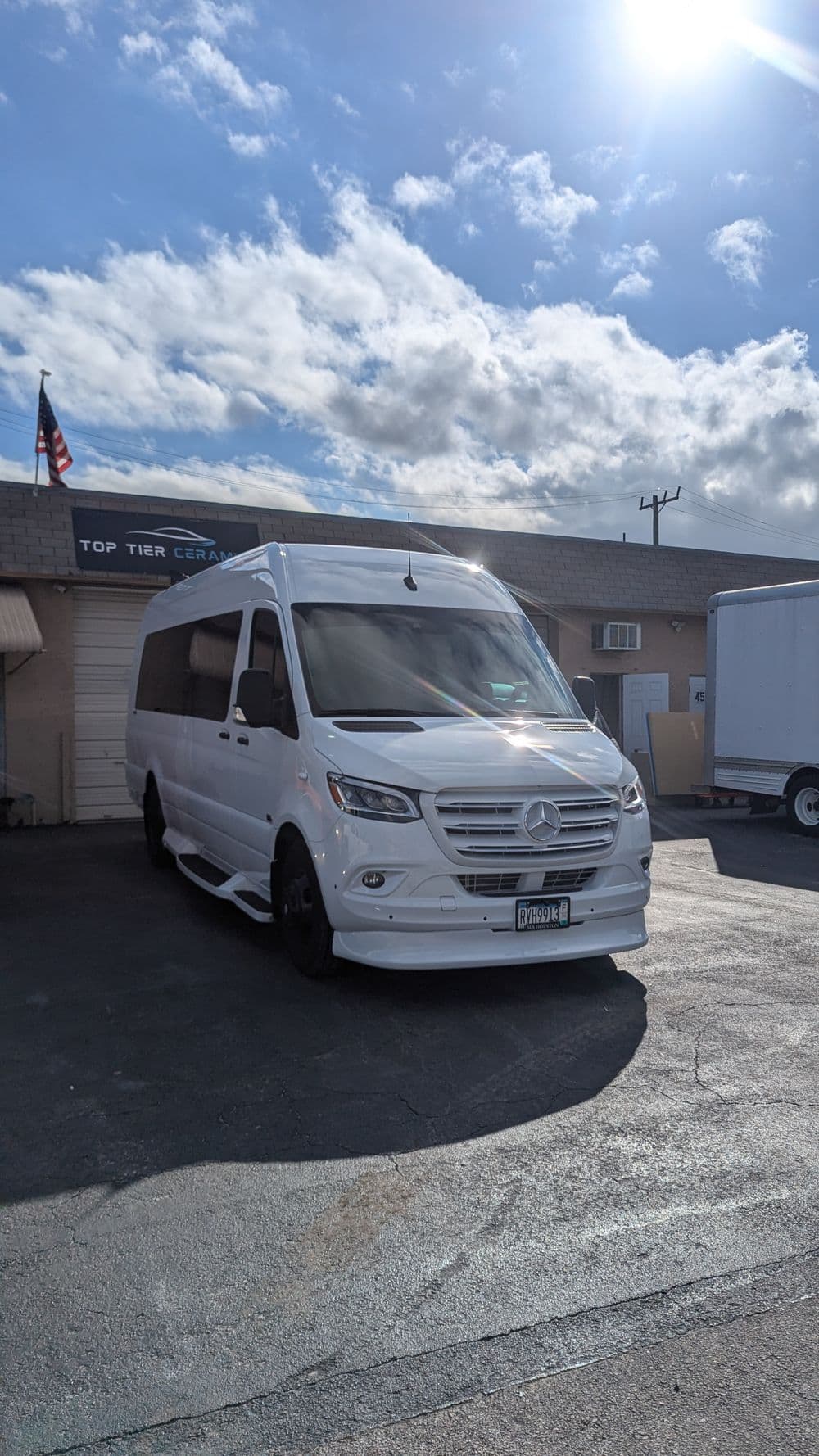 White Mercedes Sprinter van parked outside a building with blue sky and clouds.