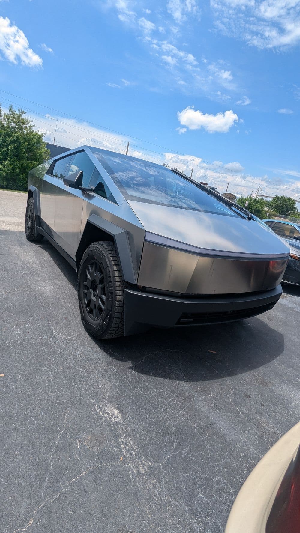 Tesla Cybertruck parked outdoors under a blue sky with clouds, showcasing its futuristic design.