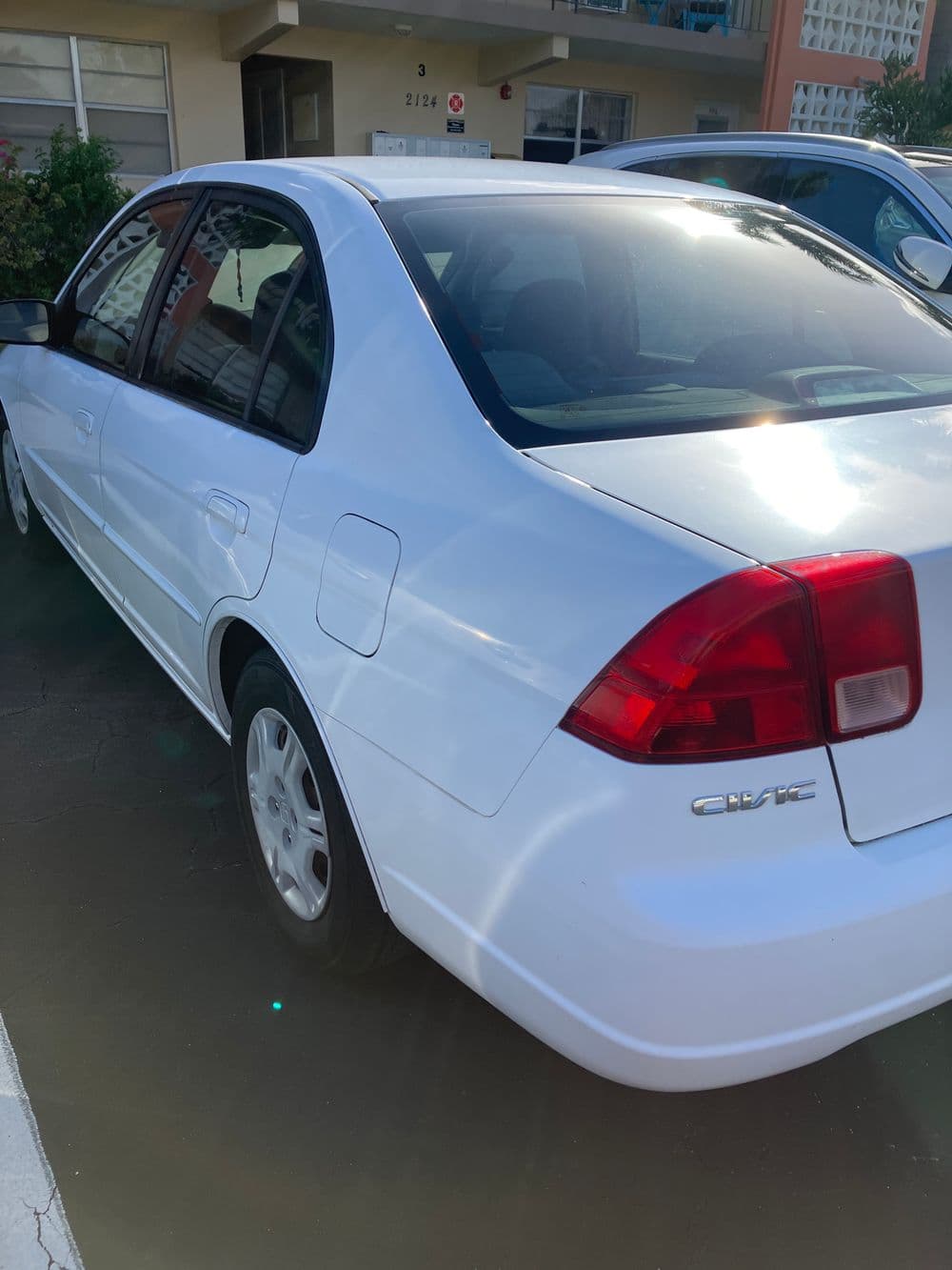White Honda Civic parked in a lot, showcasing its sleek design and sunlight reflections.