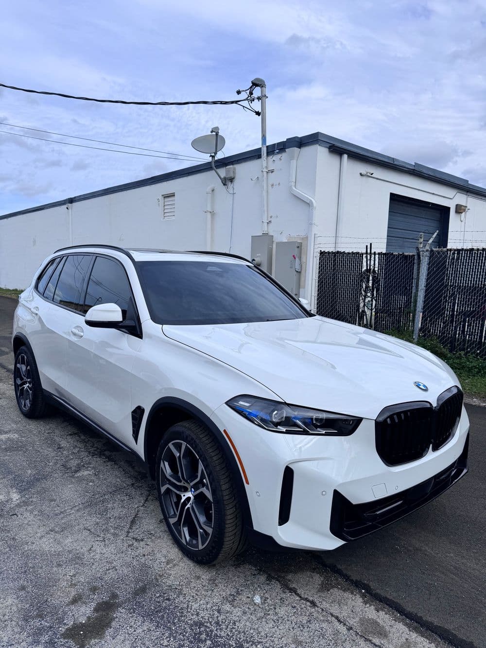 White BMW X5 parked in an industrial area with a cloudy sky in the background.