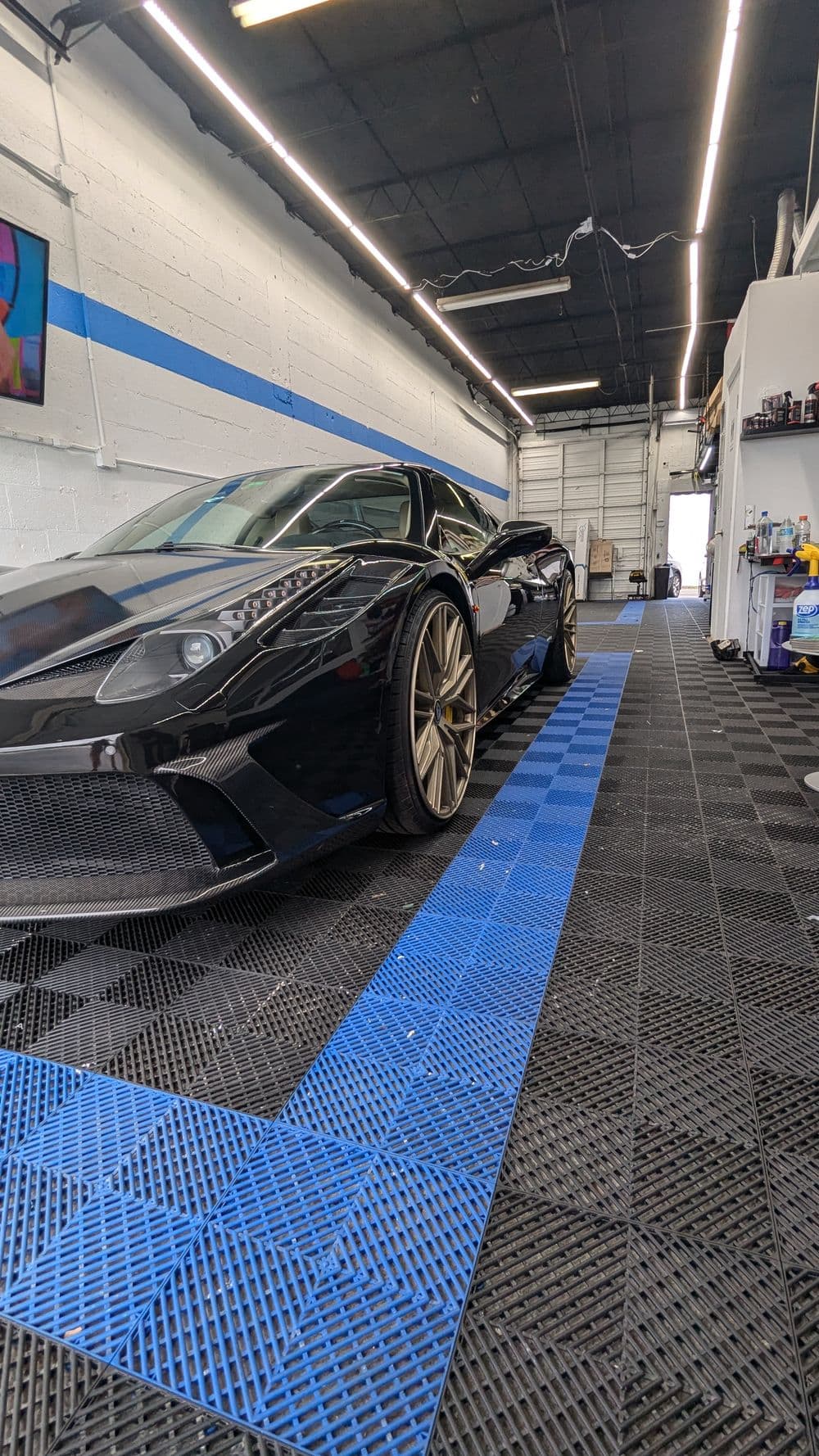 Lamborghini sports car in sleek black, displayed in a modern garage with blue floor tiles.