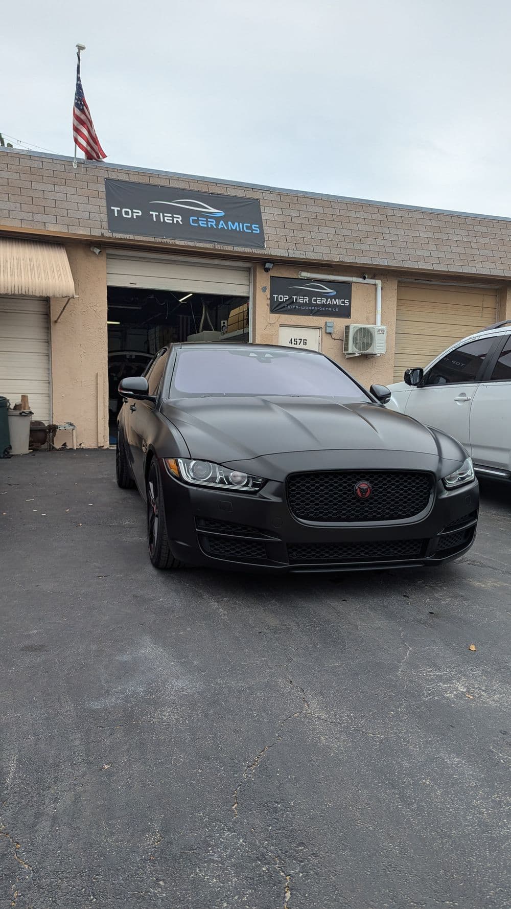 Matte black Jaguar parked in front of Top Tier Ceramics shop with an American flag.