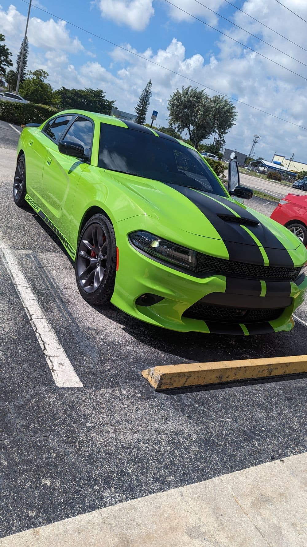 Bright green Dodge Charger with black racing stripes parked in a lot under a blue sky.