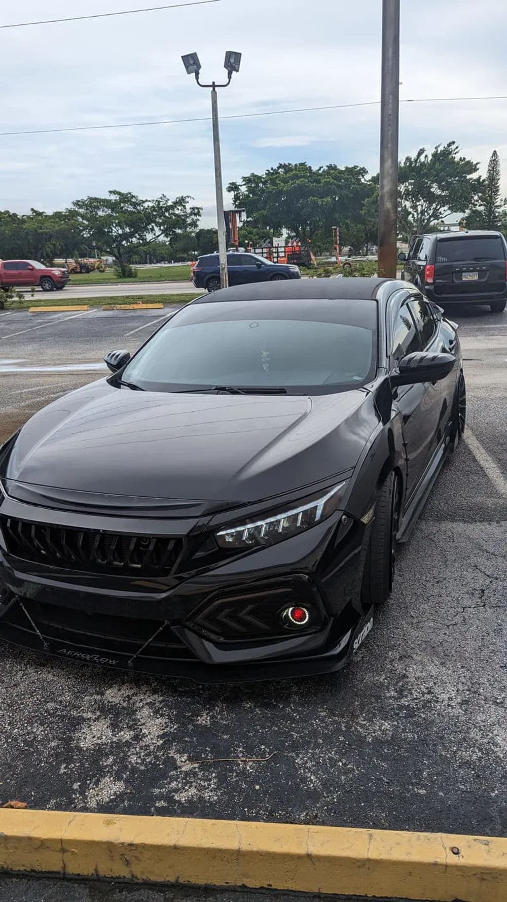 Black sports car with sleek design, positioned in a parking lot with trees in the background.