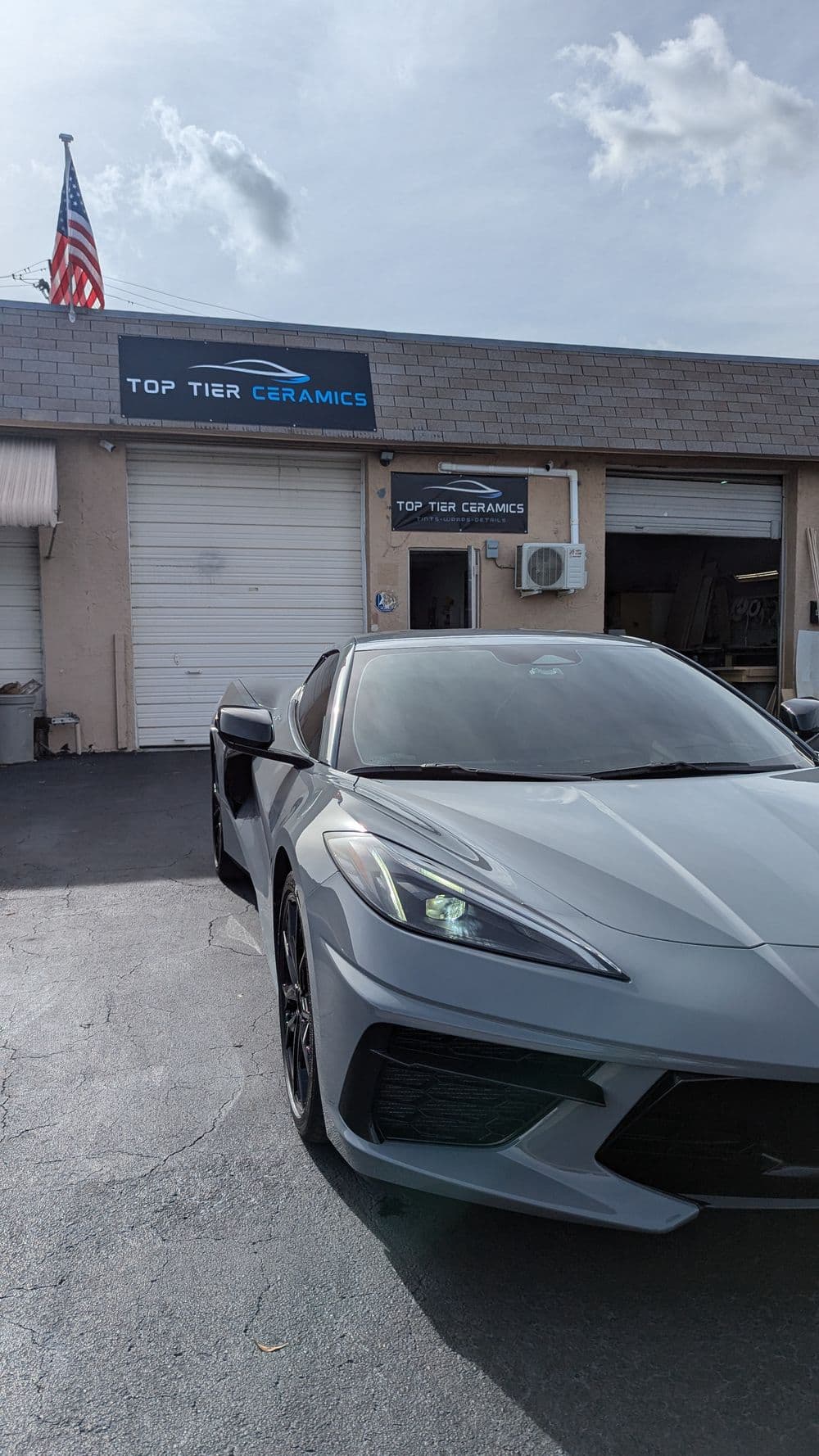 Silver sports car parked in front of Top Tier Ceramics shop with American flag.