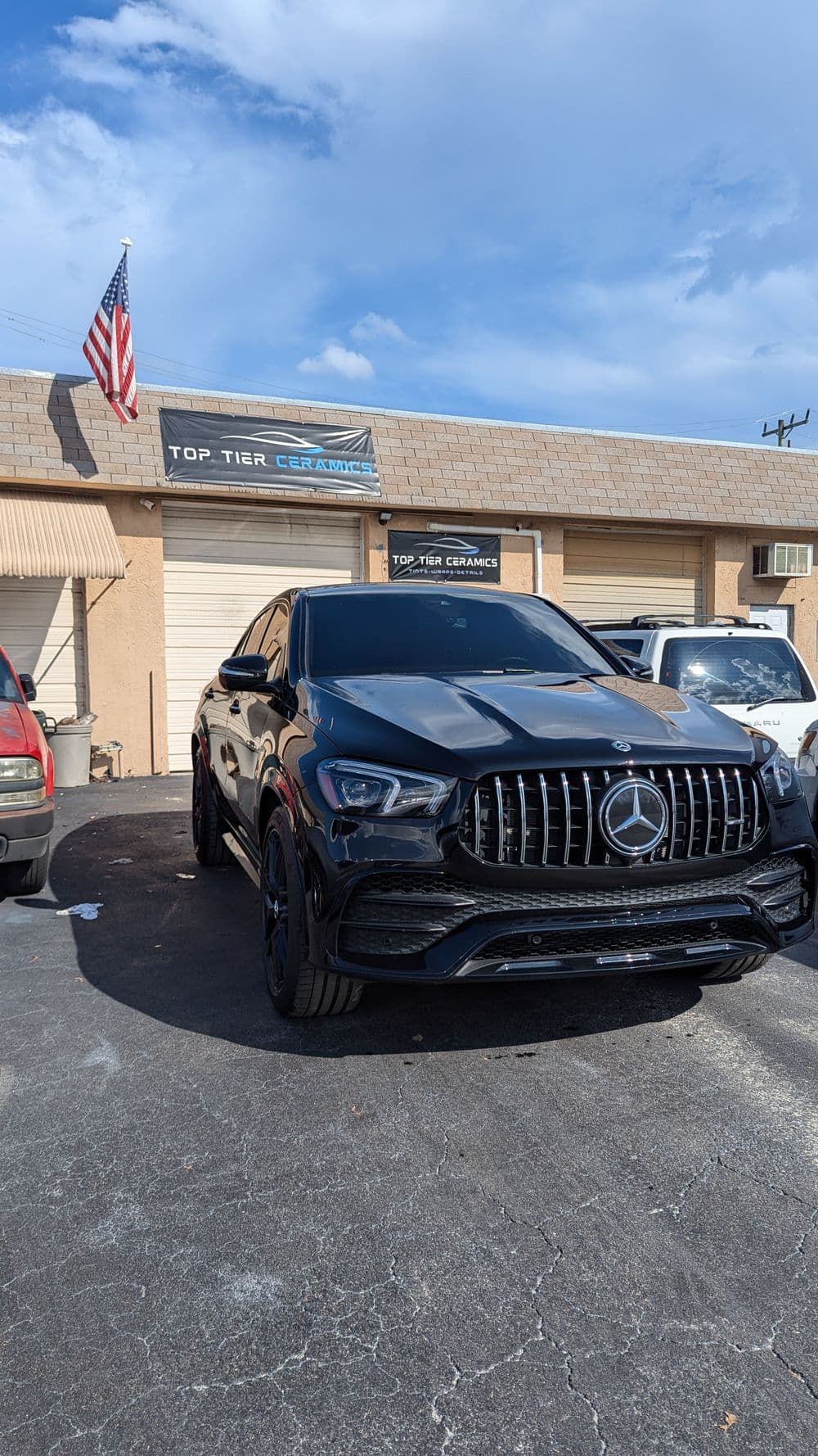 Black Mercedes parked in front of Top Tier Ceramics shop under a clear blue sky.